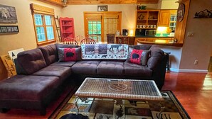 A cozy living room with a sectional sofa, a coffee table with a bear-themed rug, and a kitchen in the background.