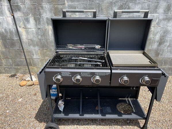 Una parrilla de gas portátil con cuatro quemadores, una repisa lateral y un número de línea de servicio al cliente.
