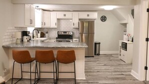 Cucina con mobili bianchi, frigorifero in acciaio inox, forno integrato e angolo bar con sgabelli.