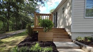 Una casa con una veranda in legno, un piccolo giardino con diverse piante e un vialetto in cemento che conduce all'ingresso.
