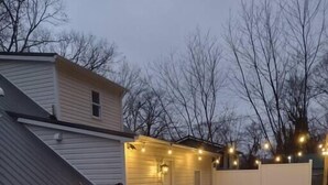 Una vasca idromassaggio in un giardino sul retro, con una casa, illuminazione esterna e un'area salotto coperta.