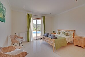 A bedroom with a bed, a nightstand, a chair, a bench, and a view of a pool through a glass door. - This villa is perfect for the holiday of a lifetime with friends or family (Alte)