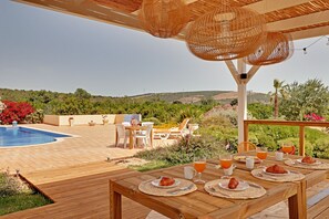 A wooden deck with a pool, outdoor furniture, and a table set for breakfast with croissants and orange juice. - This villa is perfect for the holiday of a lifetime with friends or family (Alte)