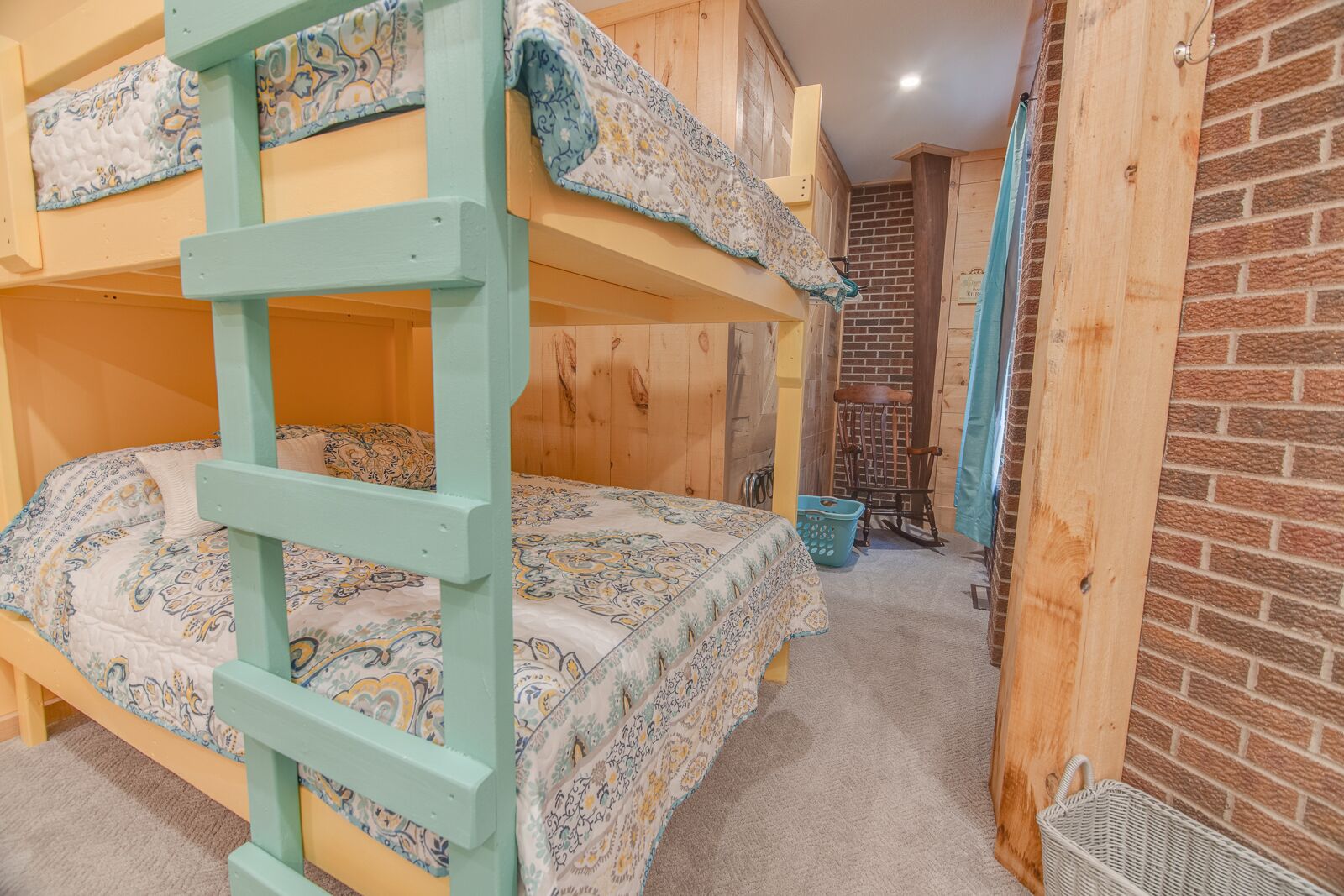 Camera con letto a castello, scala, copripiumino decorato e parete in mattoni.