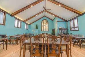 A dining area with wooden tables and chairs, a large stained glass window, and a ceiling fan. - Gathering families, friends, & coworkers (Clear Lake)