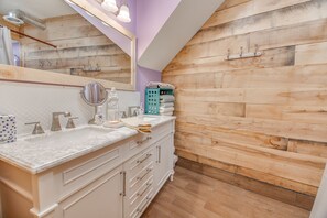 A bathroom with a wooden wall, a white vanity with a marble countertop, and a mirror. - Gathering families, friends, & coworkers (Clear Lake)