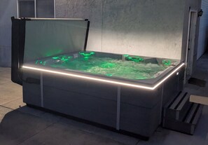 A rectangular hot tub with a glass enclosure and illuminated edges, set against a concrete wall. - Mountain View home, spacious, sleeps 12 (West Jordan)