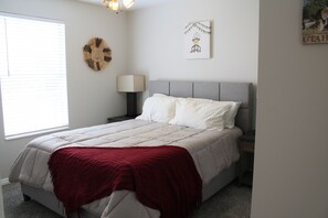 A bedroom with a bed, a nightstand, a lamp, and a wall decoration.