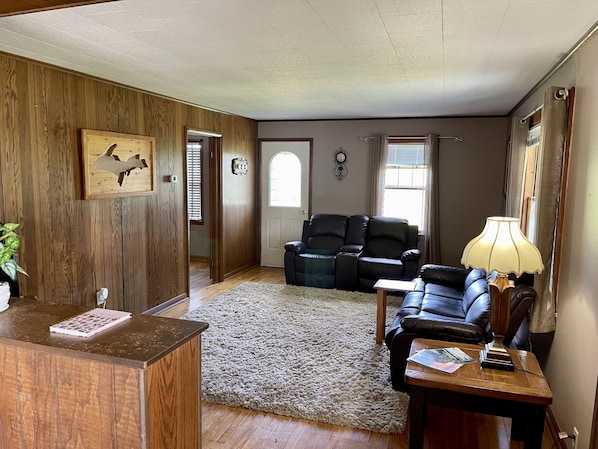 A living room with a wooden wall, a black leather sofa, a wooden coffee table, and a lamp.