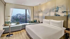 A modern hotel room with a large bed, a seating area with a view of the city, and a small table. - Park Inn by Radisson Surat (Surat)