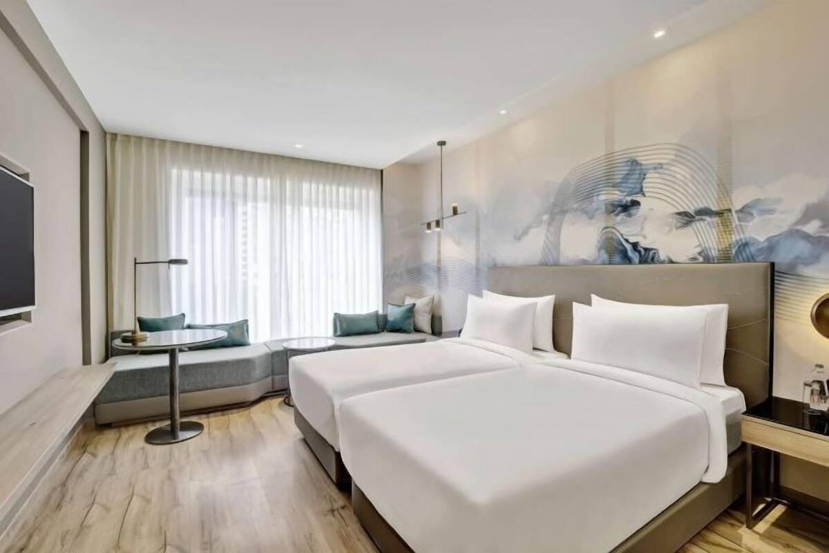 A hotel room with two beds, a seating area, a large artwork on the wall, and a television on the left.