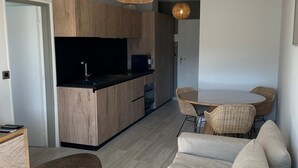 Un salon moderne comprenant un canapé, une table à manger avec des chaises, et un coin cuisine doté de meubles en bois et d’un plan de travail noir.