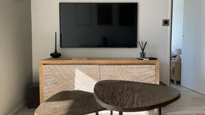 Un salon moderne avec un téléviseur à écran plat fixé au mur, une console en bois, deux fauteuils ronds et un tapis à motifs.