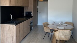 Une cuisine moderne avec des meubles en bois, un plan de travail noir et un coin repas comprenant des chaises en osier et une table ronde.