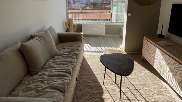 Un salon moderne avec un canapé, une petite table et une grande fenêtre donnant sur des immeubles.