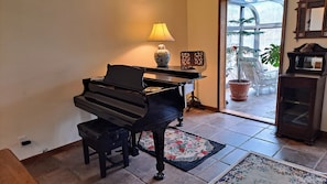 Een piano in een kamer met een lamp, een vloerkleed en een plant in pot.