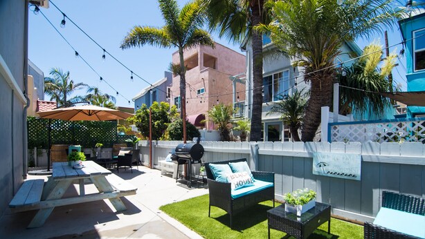 A backyard with a picnic table, outdoor furniture, a grill, and a welcome sign.