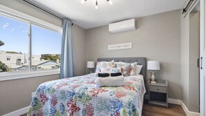 A bedroom with a bed, a nightstand, a window, and an air conditioning unit.