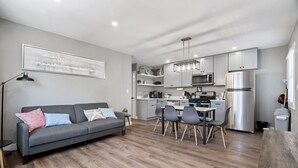 A modern kitchen with grey cabinets, stainless steel appliances, and a dining area with a grey table and chairs.