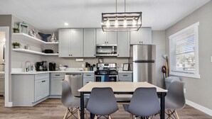 A modern kitchen with grey cabinets, a stainless steel refrigerator, a microwave, and a dining table with four chairs.