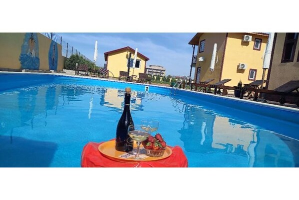 A swimming pool with a table set for a drink and fruit, surrounded by buildings.