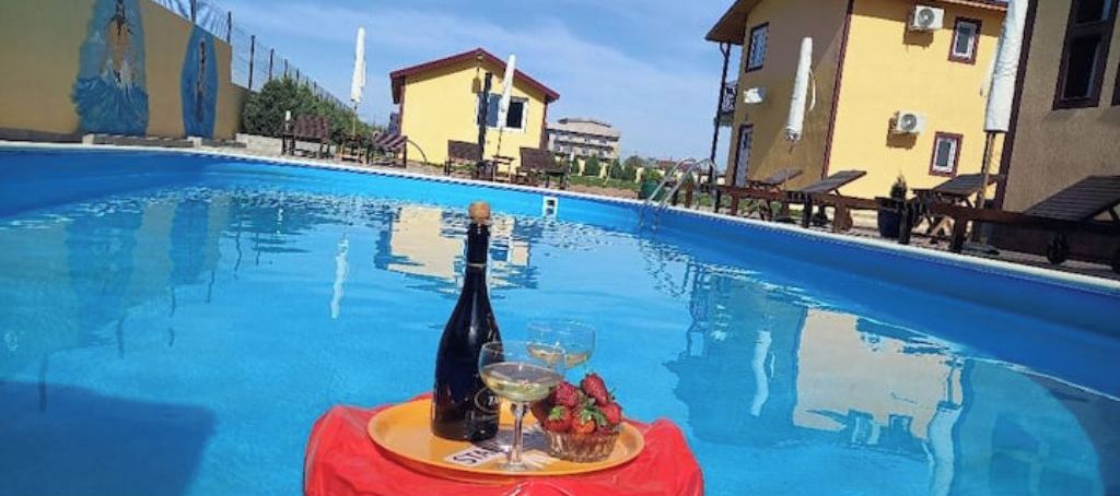 A swimming pool with a table set for a drink and fruit, surrounded by buildings.
