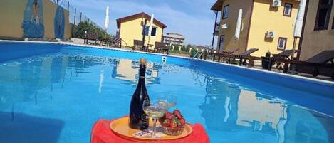 A swimming pool with a table set for a drink and fruit, surrounded by buildings.