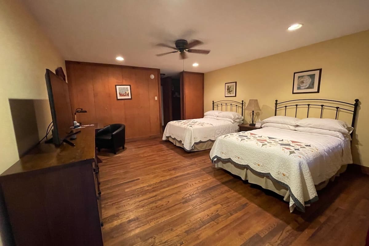 A bedroom with two single beds, a ceiling fan, wooden flooring, and a desk with a chair.