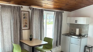 A compact kitchen with a dining table and chairs, a small refrigerator, and a trash bin. - New Hope Lodge (New Hope)