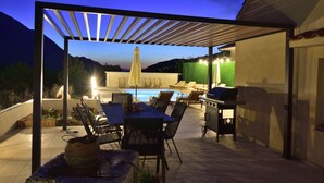 An outdoor patio with a pool, seating, and a grill area.