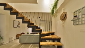 A modern interior with a wooden staircase, a grey sofa, and a wall-mounted shelf with a hat and candles.