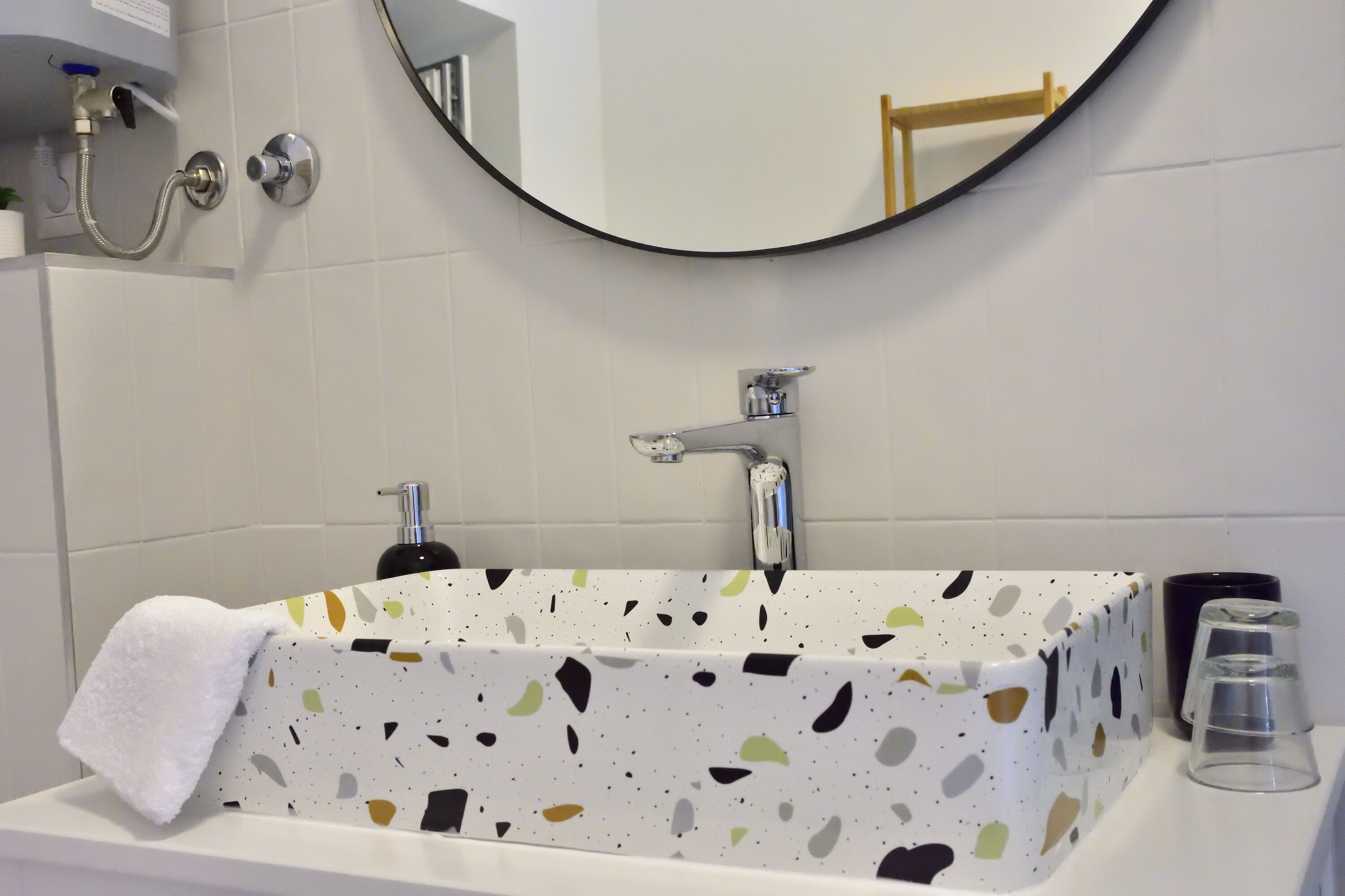 Een badkamer met een rechthoekig bad, een ronde spiegel en een handdoek aan de rand.