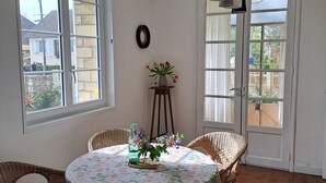 Un comedor con sillas de mimbre, una mesa redonda con mantel floral y un jarrón con flores.
