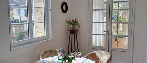 A dining area with wicker chairs, a round table with a floral tablecloth, and a vase with flowers.