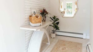 Un baño moderno con pared de ladrillo blanco, tocador blanco con cesta tejida, planta en maceta y alfombra estampada.