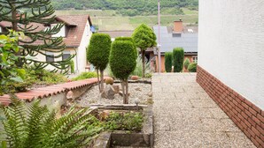 Un jardin avec des haies soigneusement taillées, un petit étang et un sentier menant à un bâtiment doté d’un toit en pente.