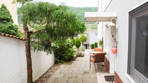 Un petit patio extérieur étroit, doté d’un sol en pierre, d’une petite table avec des chaises et d’une plante en pot.