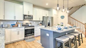 Una cocina moderna con gabinetes blancos, electrodomésticos de acero inoxidable y una isla central con taburetes de bar.