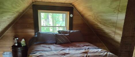 A cozy attic bedroom with a bed, pillows, a nightstand, and a window.