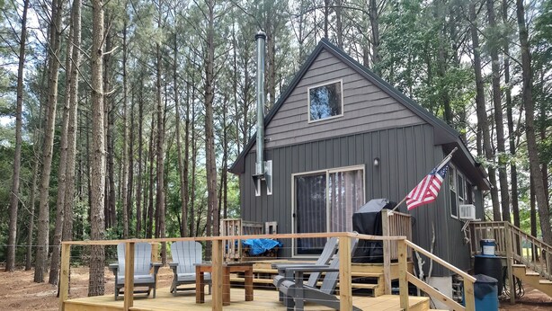 A cabin with a deck, outdoor seating, and an American flag. - Awesome private off grid cabin with creek view. (Onancock)