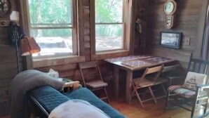 A cozy cabin room with a bed, a small table, and a window. - Awesome private off grid cabin with creek view. (Onancock)