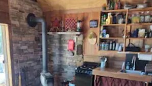 A rustic cabin interior with a wooden ceiling, stone walls, a fireplace, and a dining area with shelves. - Awesome private off grid cabin with creek view. (Onancock)