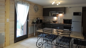 A compact kitchen with a dining area, featuring a wooden interior, a clock on the wall, and basic appliances. - Studio for 6 with terrace and private parking (Valloire)