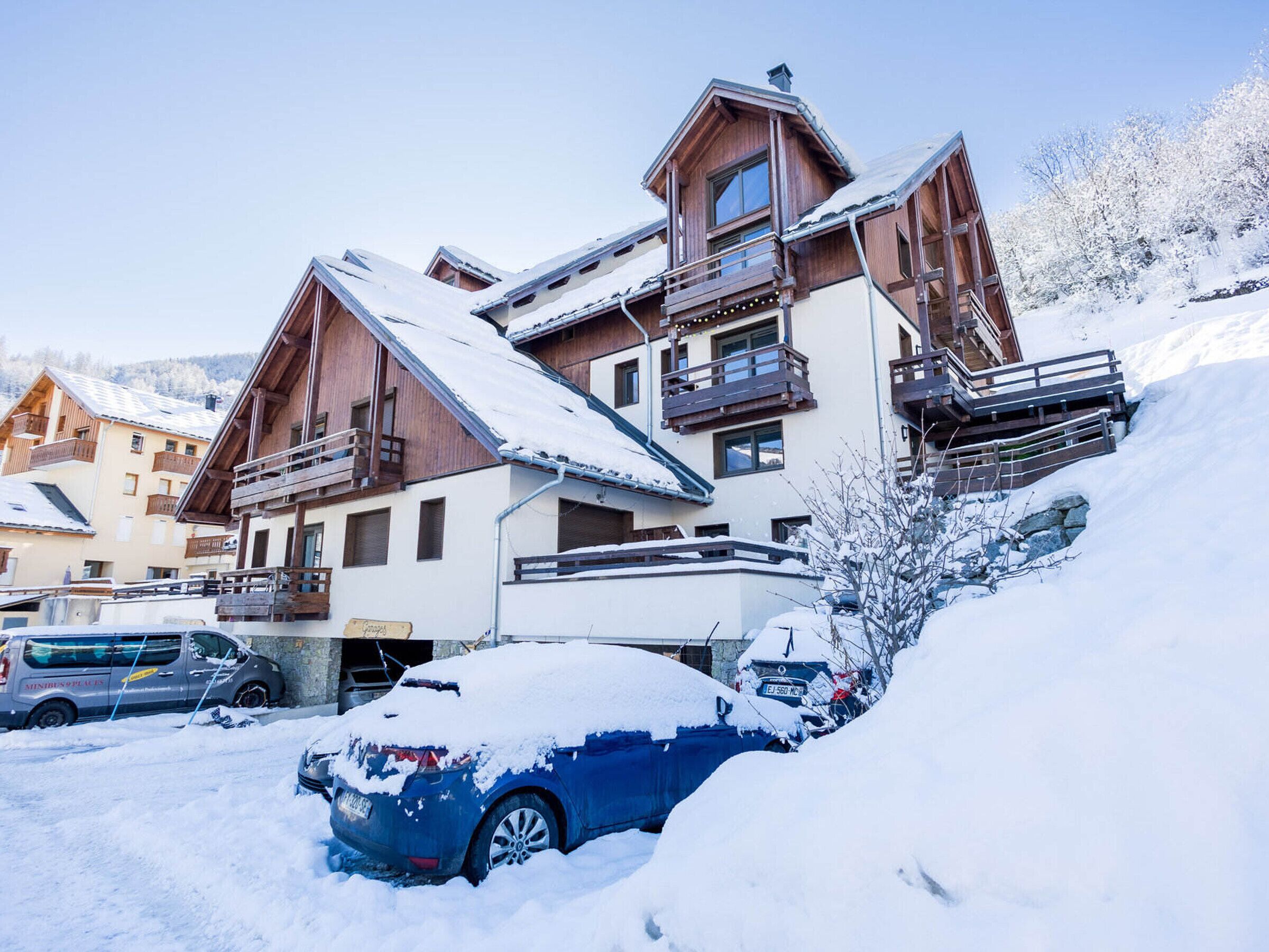 Un edificio de varios pisos con balcones, un telesilla y un paisaje cubierto de nieve.