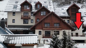 A multi-story building with a sloped roof, wooden balconies, and a red arrow pointing downwards. - Studio for 6 with terrace and private parking (Valloire)