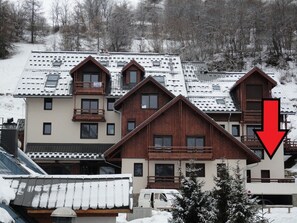 Ein mehrstöckiges Gebäude mit einem geneigten Dach, hölzernen Balkonen und einem roten Pfeil, der nach unten zeigt.
