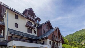 A multi-story building with balconies, a stone foundation, and a sign indicating a restaurant. - Studio for 6 with terrace and private parking (Valloire)