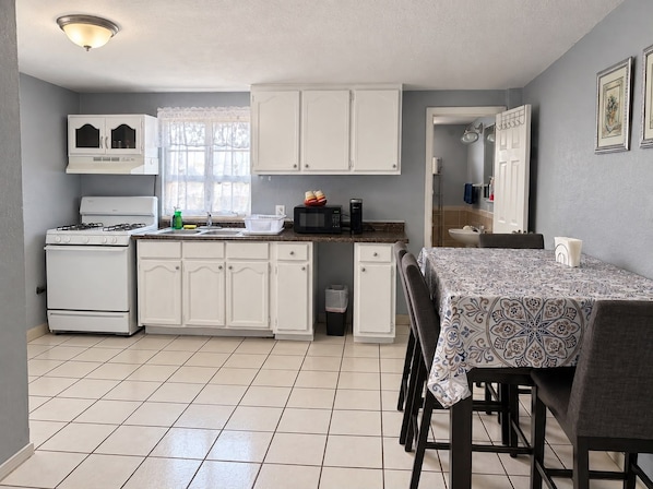 A compact kitchen with white cabinets, a stove, and a dining area with a table and chairs. - Del Sol Medical Center Gem (El Paso)