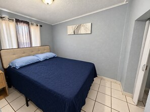 A bedroom with a bed, curtains, a wall-mounted artwork, and a door. - Del Sol Medical Center Gem (El Paso)