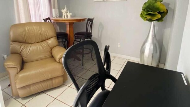 A living room with a sofa, a dining table with chairs, a vase with a plant, and a painting on the wall. - Del Sol Medical Center Gem (El Paso)